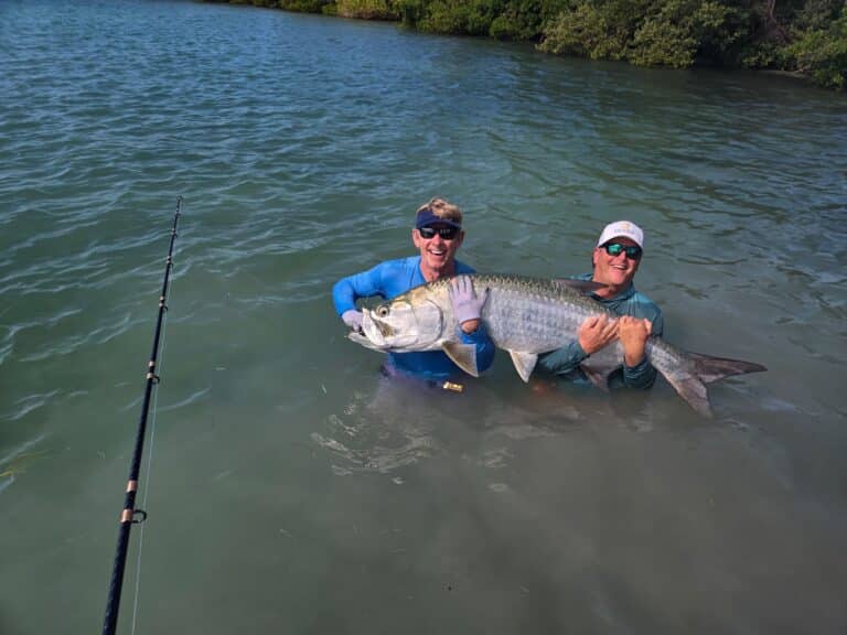 Two anglers hold a tarpon in shallow Boca Grande area water